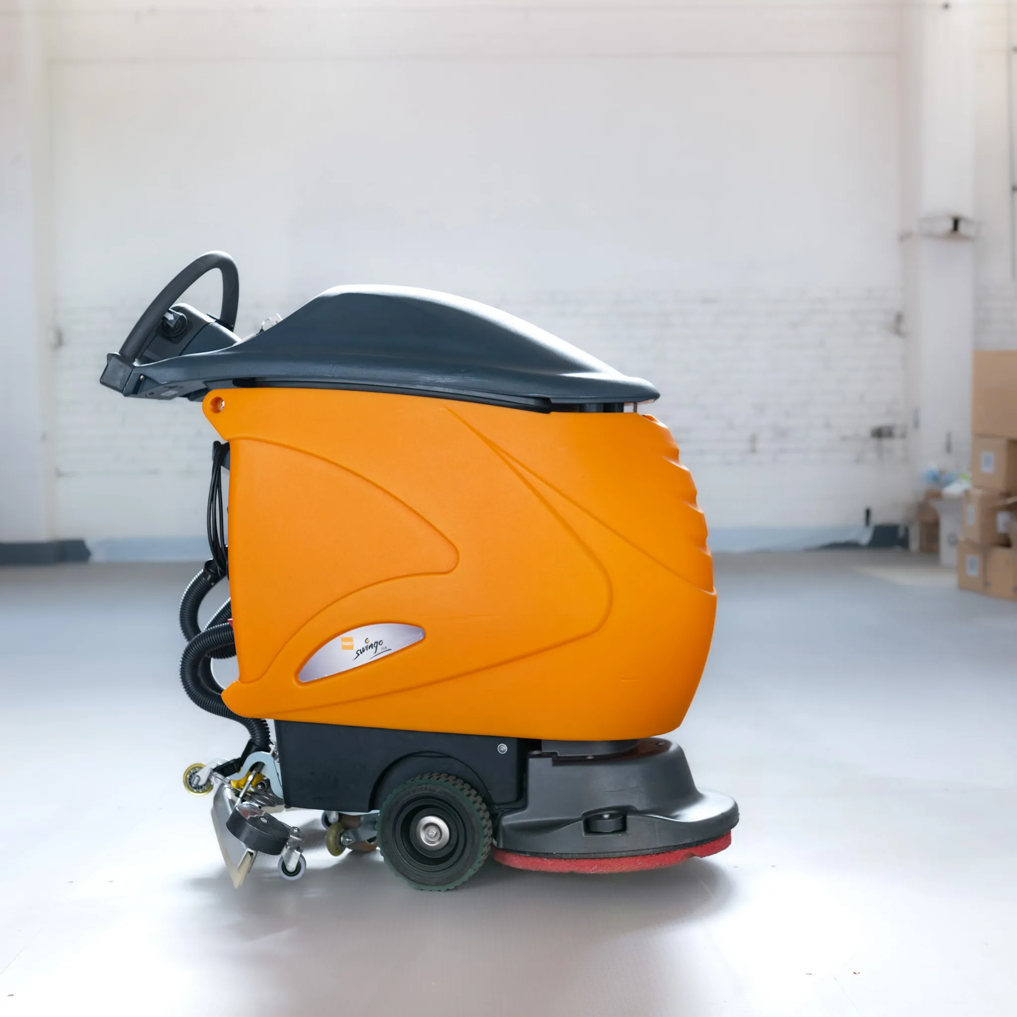 Orange Taski Swingo gåbar skurmaskin från sidan i en ljus lagerhall